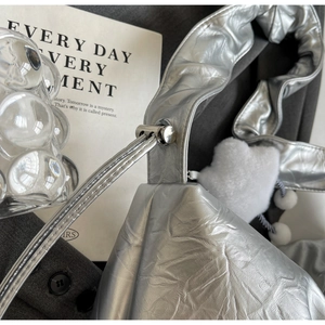 Detail of silver pleated metallic tote bag with white plush heart charm and metal buckle