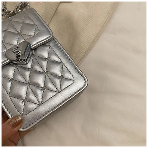 Detail of silver quilted phone bag featuring heart clasp and metallic chain strap