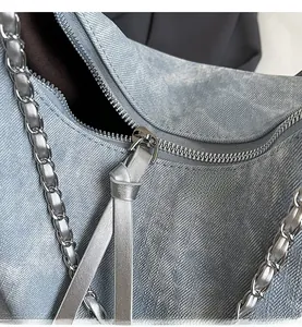 Close-up of smooth silver zipper and chain strap on blue denim hobo shoulder bag