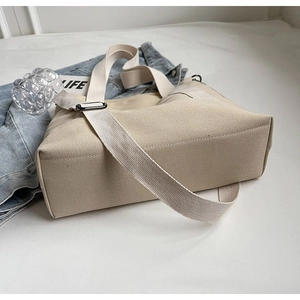 Detail of beige canvas tote bag showing adjustable strap and large capacity side zipper