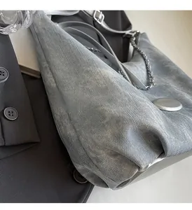 Detail of grey denim tote bag with silver chain strap and metal clasp on grey blazer