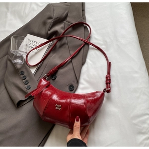 Détail macro du sac demi-lune rouge vin avec cuir brillant et logo argenté chic