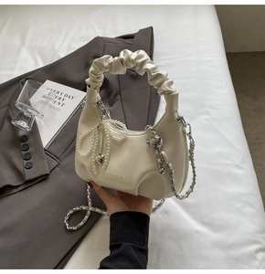 Détail du sac plissé blanc cassé avec pendentif nœud perlé et bandoulière chaîne