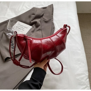 Détail du sac croissant rouge foncé avec logo métallique et coutures verticales chics