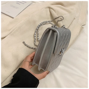 Close-up of a silver quilted crossbody bag featuring a heart clasp and chain strap