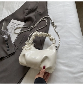 Détail du sac nuage plissé blanc cassé avec breloque perle et bandoulière sur lit