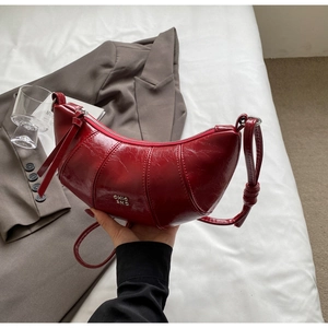 Détail du sac croissant en cuir bordeaux brillant avec logo et texture plissée