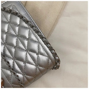 Close-up of silver quilted texture with interwoven metal chain strap on small bag