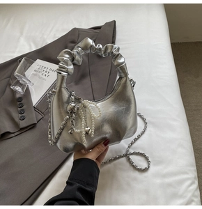 Détail du sac à main plissé argenté avec nœud en perles et pendentif cœur en métal