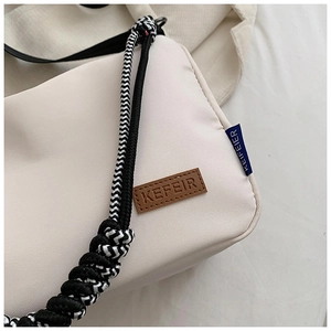Détail du sac en toile montrant le logo en cuir marron et la bandoulière tressée