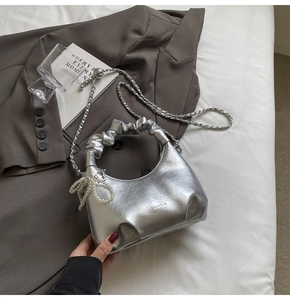 Détail d'un sac à main argenté plissé avec éclat métallique et breloque perle