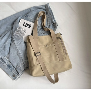 Flat lay of a khaki canvas tote bag with metal snap pockets and adjustable shoulder strap