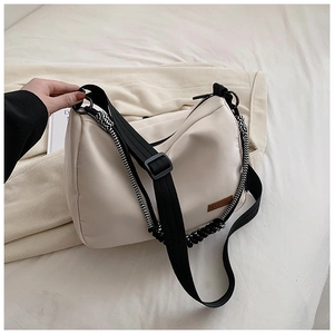 Détail du sac bandoulière en toile crème avec écusson logo marron et sangle réglable