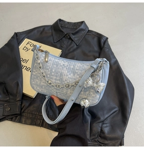 Détail du sac tressé bleu clair avec chaîne argentée et charm nœud sur veste noire