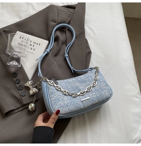 Détail du sac tissé bleu clair avec chaîne argentée et pendentif nœud sur un blazer