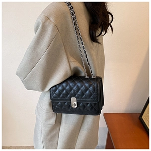 Detail of a black quilted leather crossbody bag with silver chain strap and metal lock