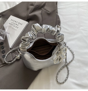 Détail du sac à main argenté plissé avec bandoulière chaîne et breloque perle nœud