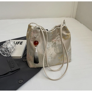 Detailed embroidery of pink plum blossoms on a cream jacquard tote with tassel charm
