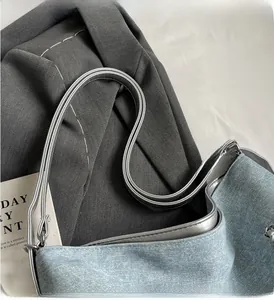 Detail of light blue denim tote with metallic silver handles and trim on grey fabric