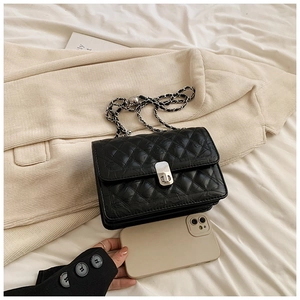 Flat lay of a black quilted chain bag next to a smartphone showing its compact size