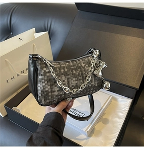 Détail du sac sous le bras tressé gris avec chaîne argentée et pendentif boule en métal