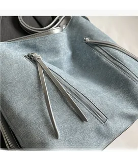 Detail of light blue denim texture and functional gray leather zipper pockets on a tote bag