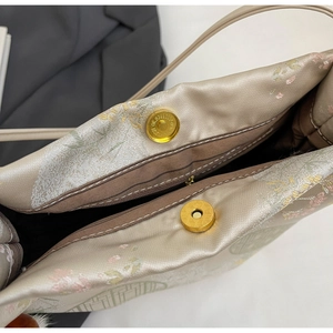 Macro shot of gold magnetic buckles and fine floral embroidery on the silk tote bag