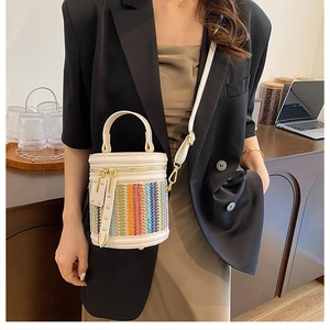 Detail of color-block straw bucket bag featuring leather handles and detachable strap