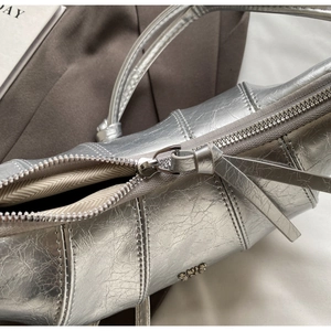 Détail du sac argenté effet cuir froissé avec logo métallique et fermeture éclair fluide