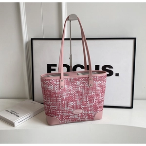 Détail du cabas tissé rose avec finitions en cuir et logo en métal sur un socle blanc