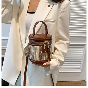 Detail of a brown leather and yellow woven bucket bag with metallic rivets and top handle
