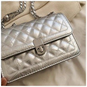 Detail of silver quilted leather texture and metallic chain strap on crossbody bag