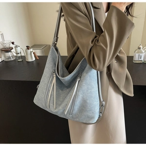 Light blue denim tote bag with silver zippers and long leather straps in a cafe setting