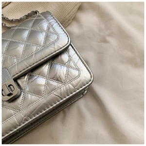 Detailed close-up of silver quilted crossbody bag with metallic chain and rotary lock