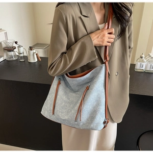 Detail of light blue denim hobo bag with brown leather trim and zipper accents