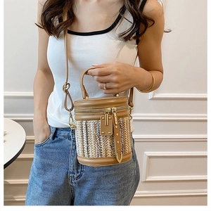 Detail of cylindrical straw bucket bag with brown leather trim and dual gold zippers
