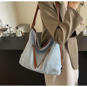 Detail view of large tote bag in light blue denim and brown leather strap on model