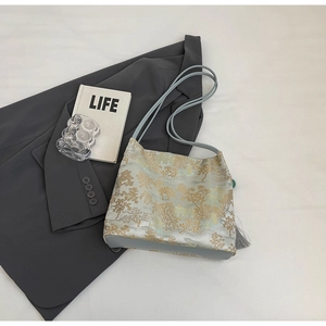 Close-up of golden Chinese landscape embroidery on a blue tote bag with grey tassel