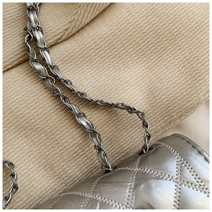 Close-up of metallic silver quilted crossbody bag with woven chain strap and fine stitching