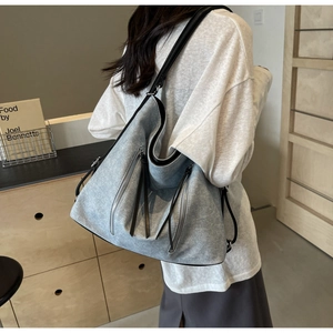 Detail of grey-blue canvas tote with silver zippers and black leather strap on model