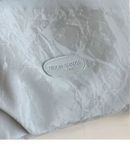 Détail du sac fourre-tout gris à texture froissée avec un patch logo MUON SHARK embossé
