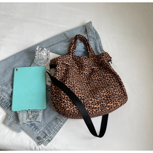 Borsa tote in tela leopardata con tracolla nera posata su un tessuto decorativo