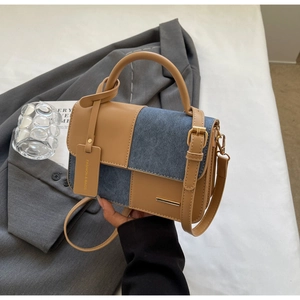 Dettaglio della borsa bicolore in pelle marrone e denim blu con elegante barra in metallo oro