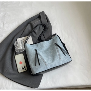 Detail of light blue denim tote bag with black leather straps and dual zipper tassels