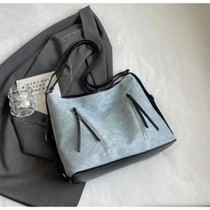 Detail of light blue denim tote with black leather trim and dual vertical zipper design