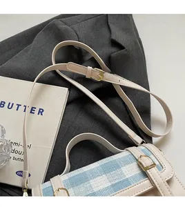 Detail of adjustable leather strap and smooth metal buckle on blue plaid crossbody bag