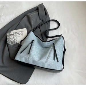 Detail of light blue denim tote bag with black leather stitching and vertical zippers