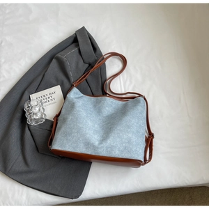 Detail of blue denim tote bag with brown leather straps on white textured fabric