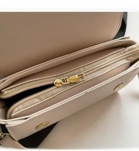 Detail of smooth gold zipper and interior compartments on beige leather crossbody bag