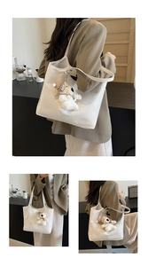 Detail of white tote bag with cute plush puppy charm and minimalist shoulder strap design